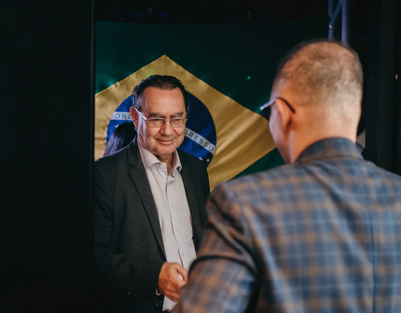 Homem sorrindo diante de uma bandeira do Brasil